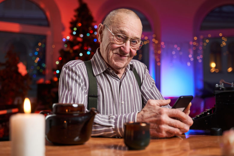 Cheerful elder man using a mobile phone sitting at table in room